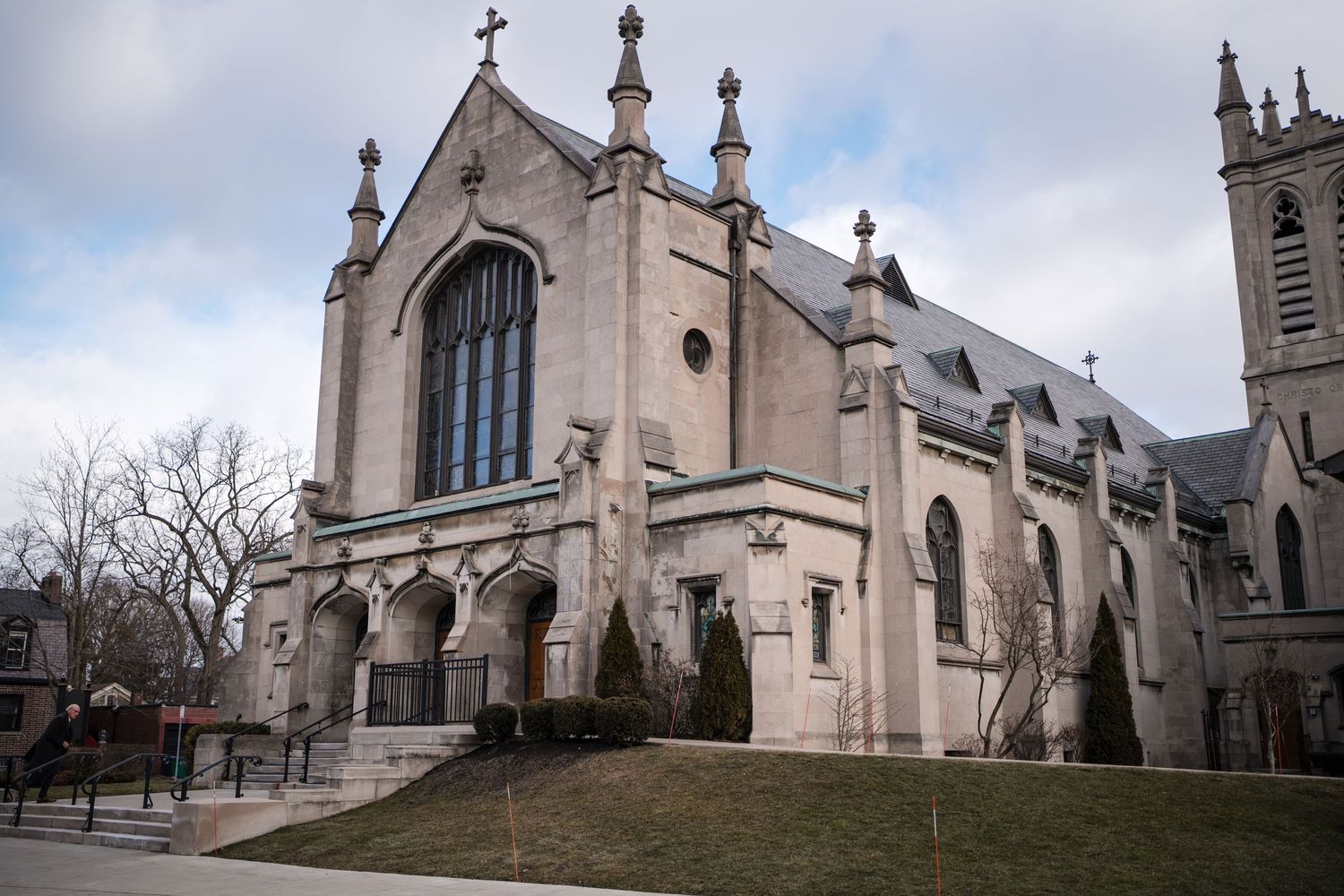 A gothic-style stone church with arched windows and spires stands against a cloudy sky.