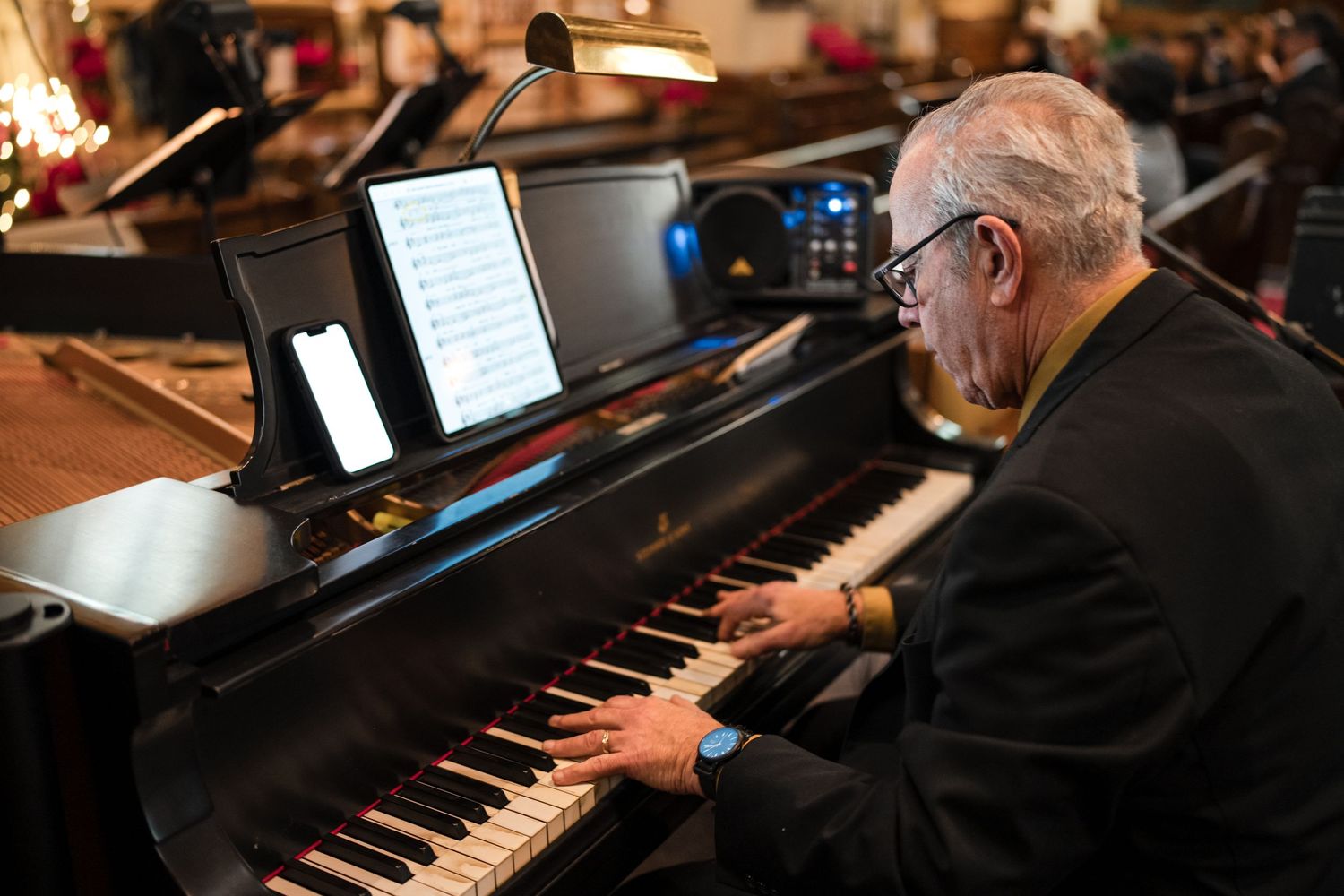 A musician plays a grand piano in a dimly lit church setting.