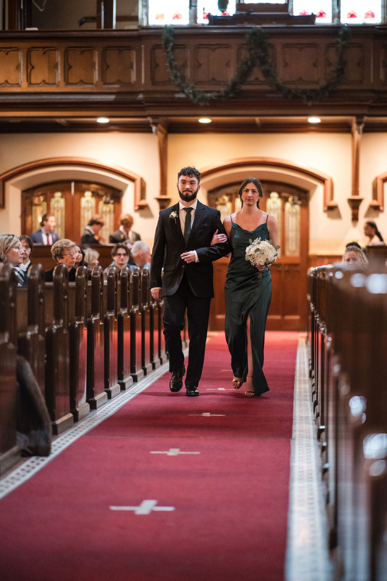 A couple walks arm in arm down the center aisle of a traditional church during a ceremony.