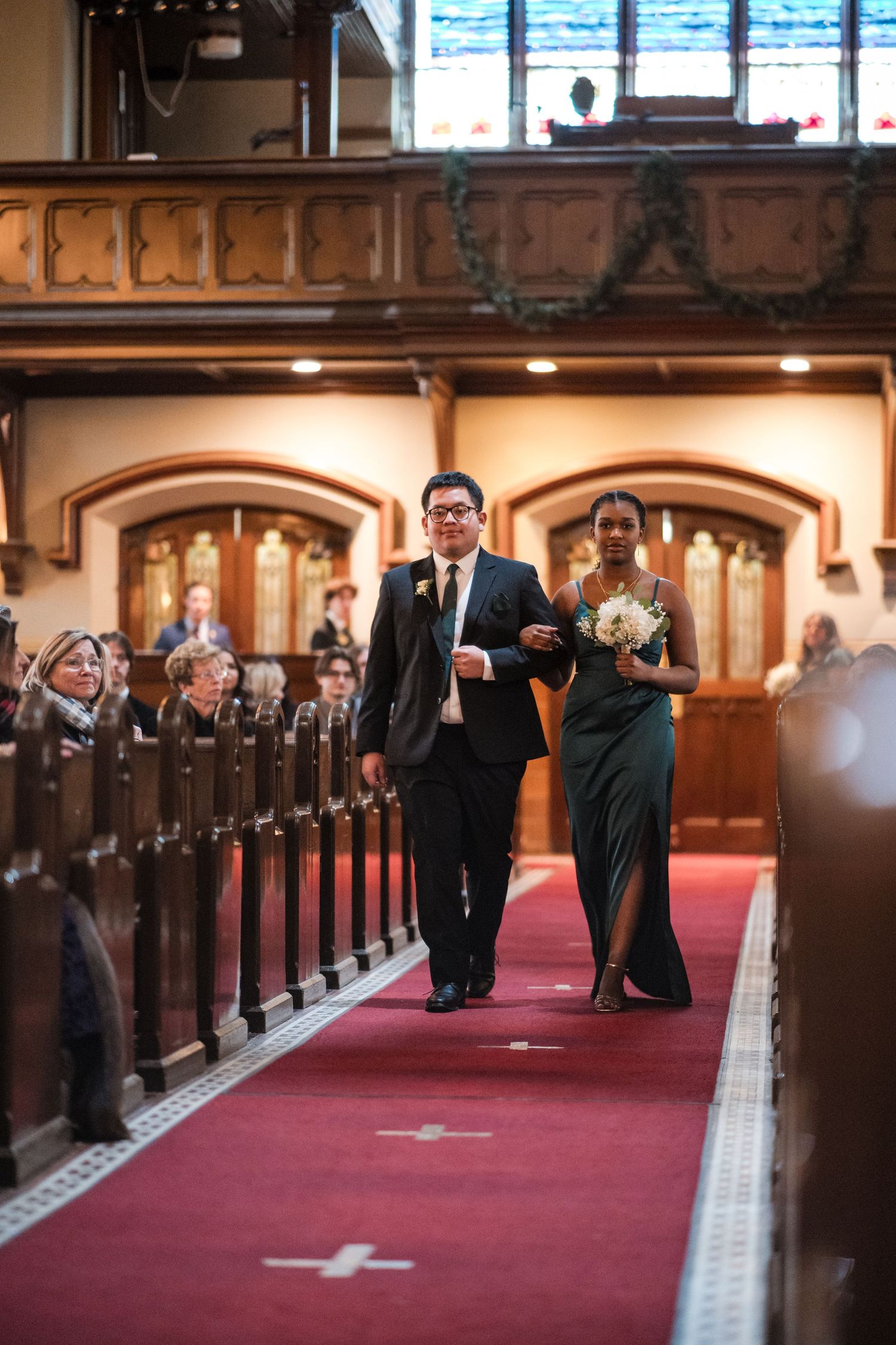 Wedding attendants proceed down a red-carpeted church aisle during a formal ceremony.