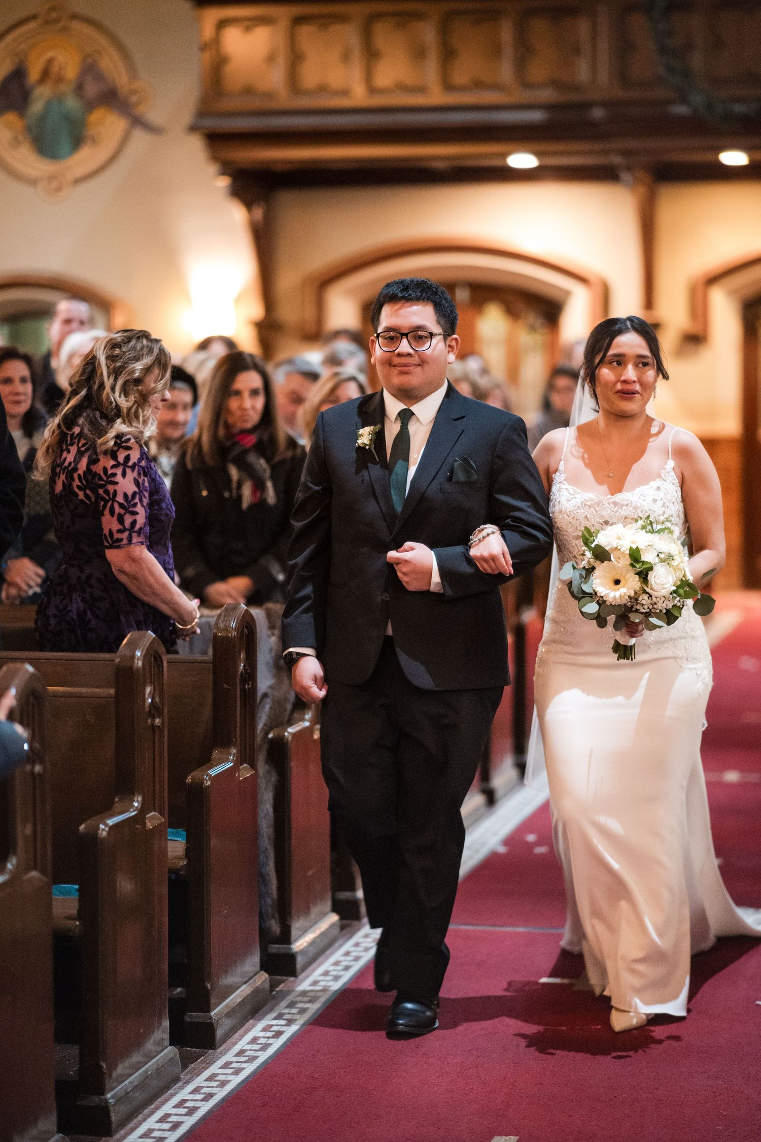 Attendees watch from wooden church pews as a couple proceeds down the red-carpeted aisle.