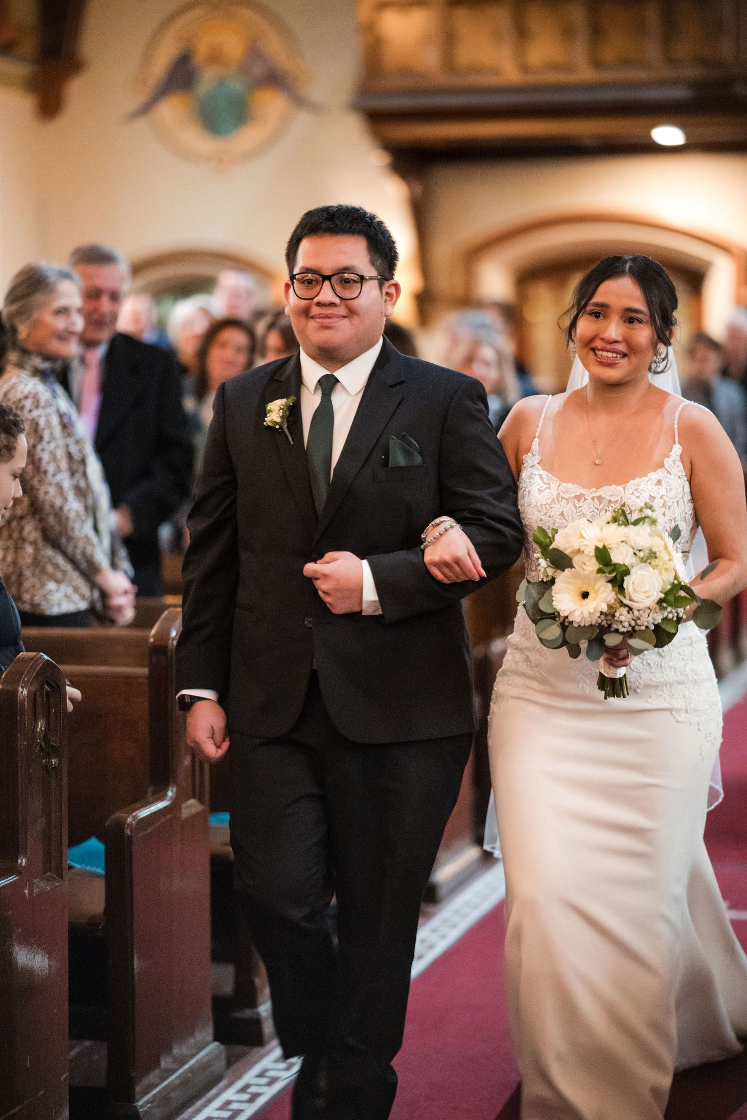 A happy couple walks arm in arm down a church aisle lined with wooden pews.