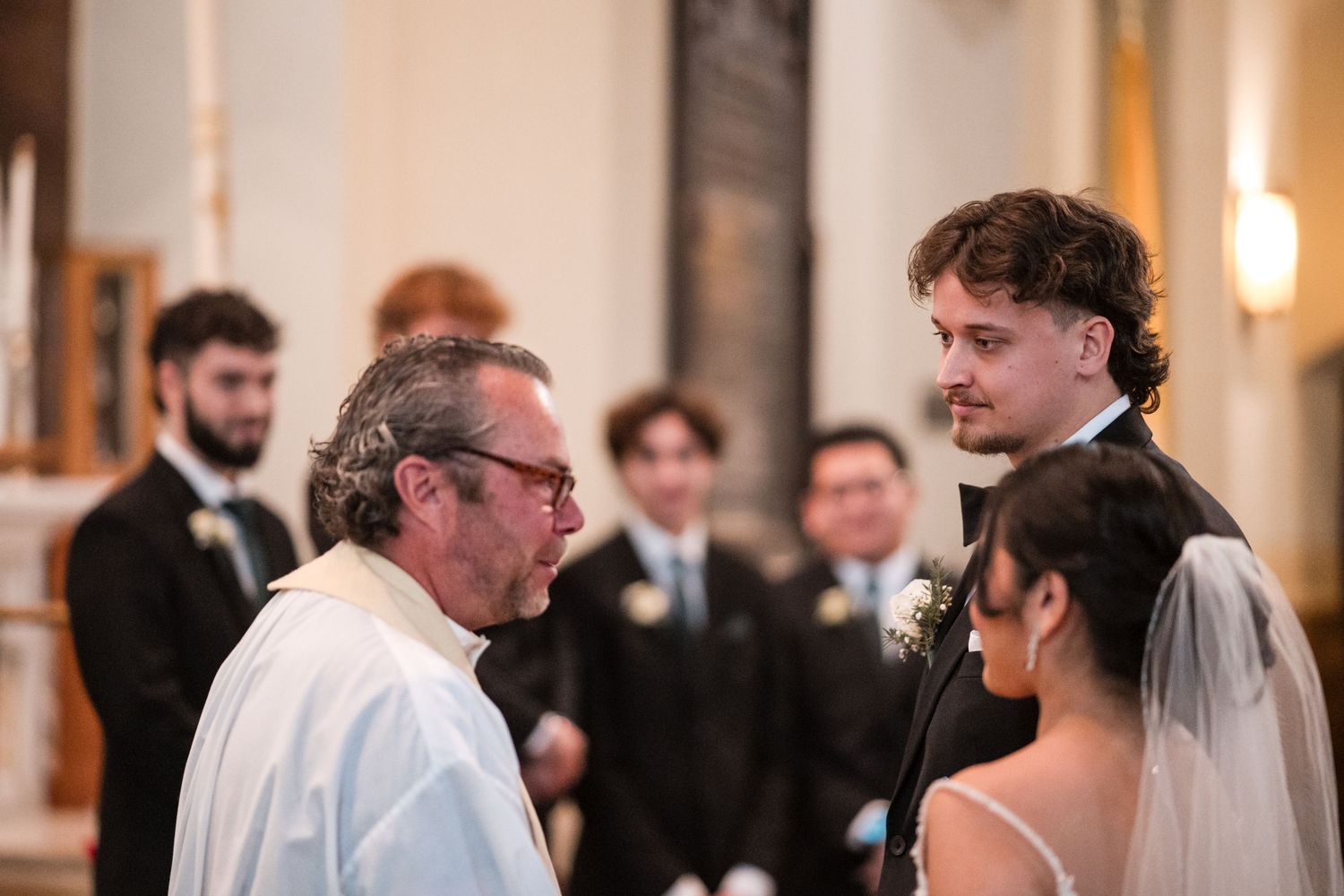 A religious officiant speaks to a couple during their wedding ceremony in a church.