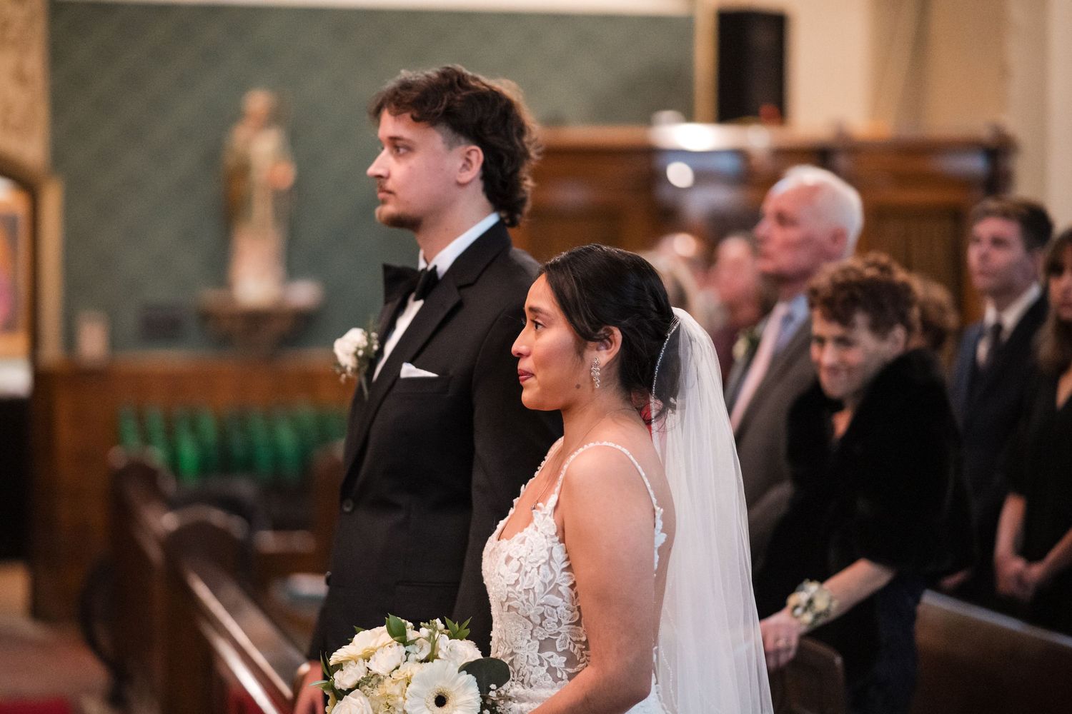 A couple stands at attention during their wedding ceremony in a traditional church setting.