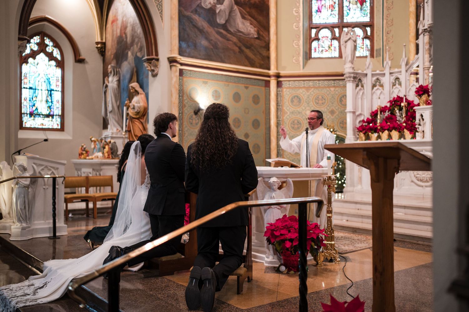 A wedding ceremony taking place in a traditional church with Gothic architecture and red poinsettia decorations.