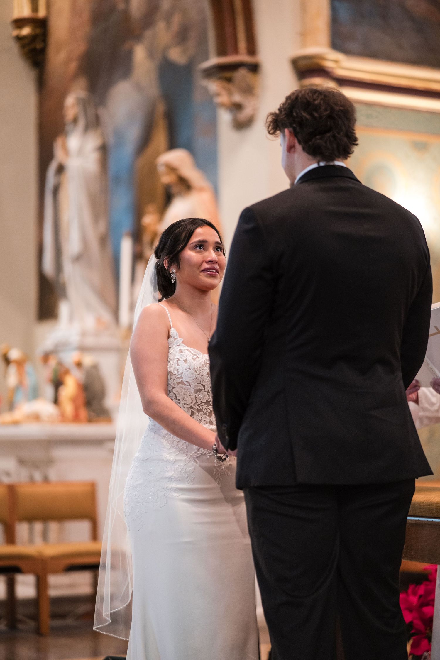 A couple exchanging vows in an elegant church setting with traditional religious artwork and architecture.