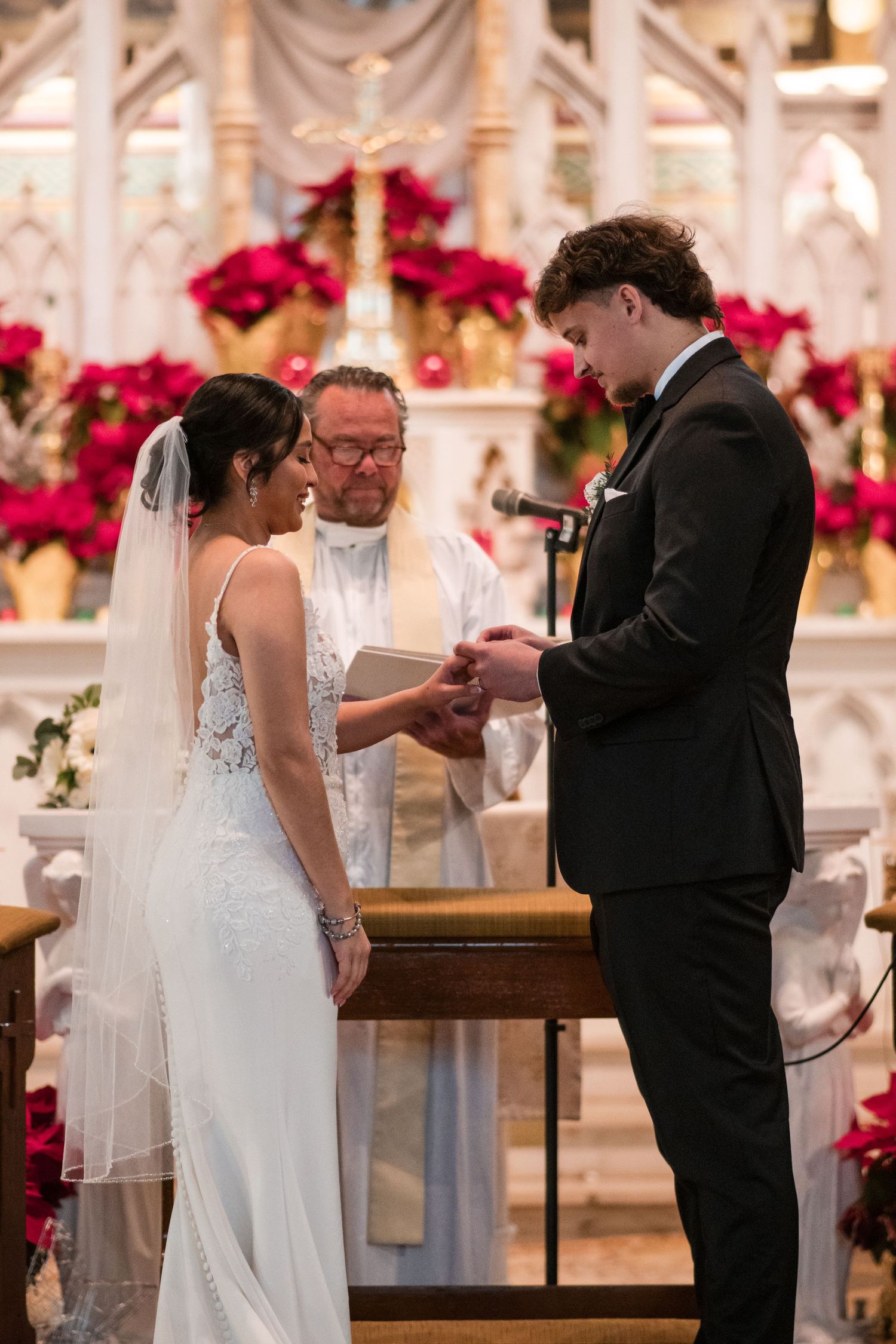 A wedding ceremony with a couple exchanging rings at the altar decorated with red poinsettias.