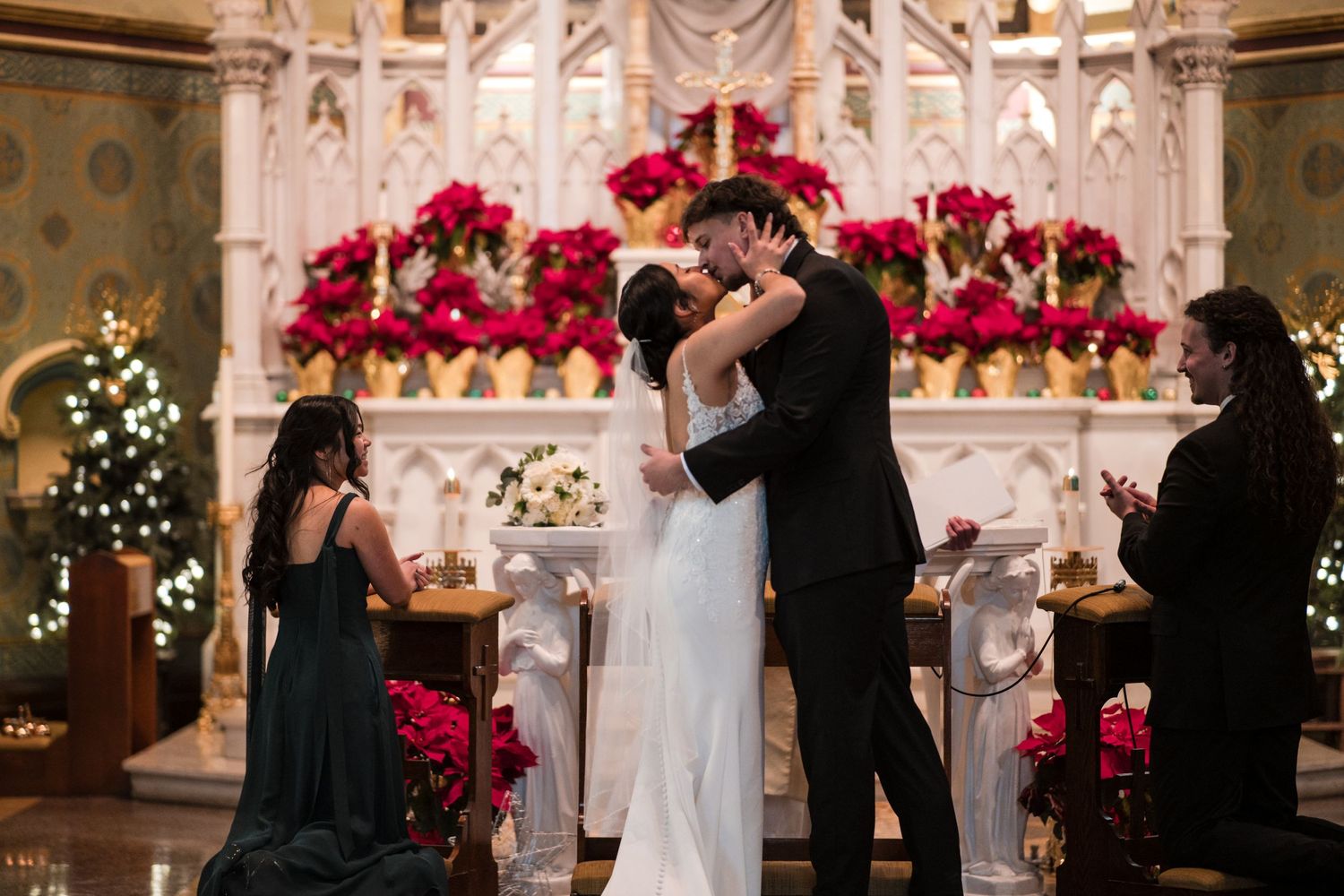 A romantic first kiss at the altar surrounded by beautiful red floral arrangements and Christmas decor.