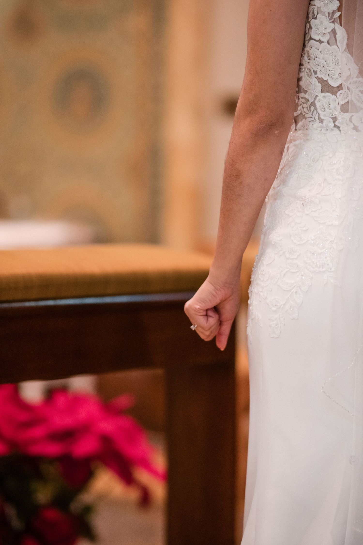 Detail shot of an elegant white lace wedding dress against a church interior.
