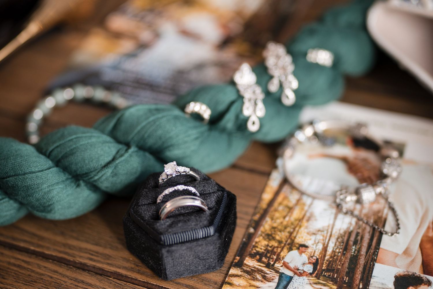 Wedding accessories including rings, jewelry, and green fabric arranged on wooden surface.