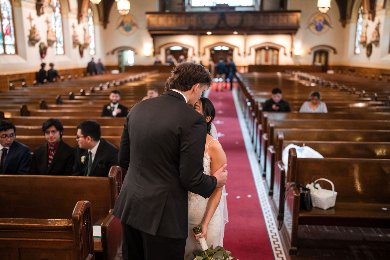 Wedding ceremony in a grand church with wooden pews and red carpet aisle.