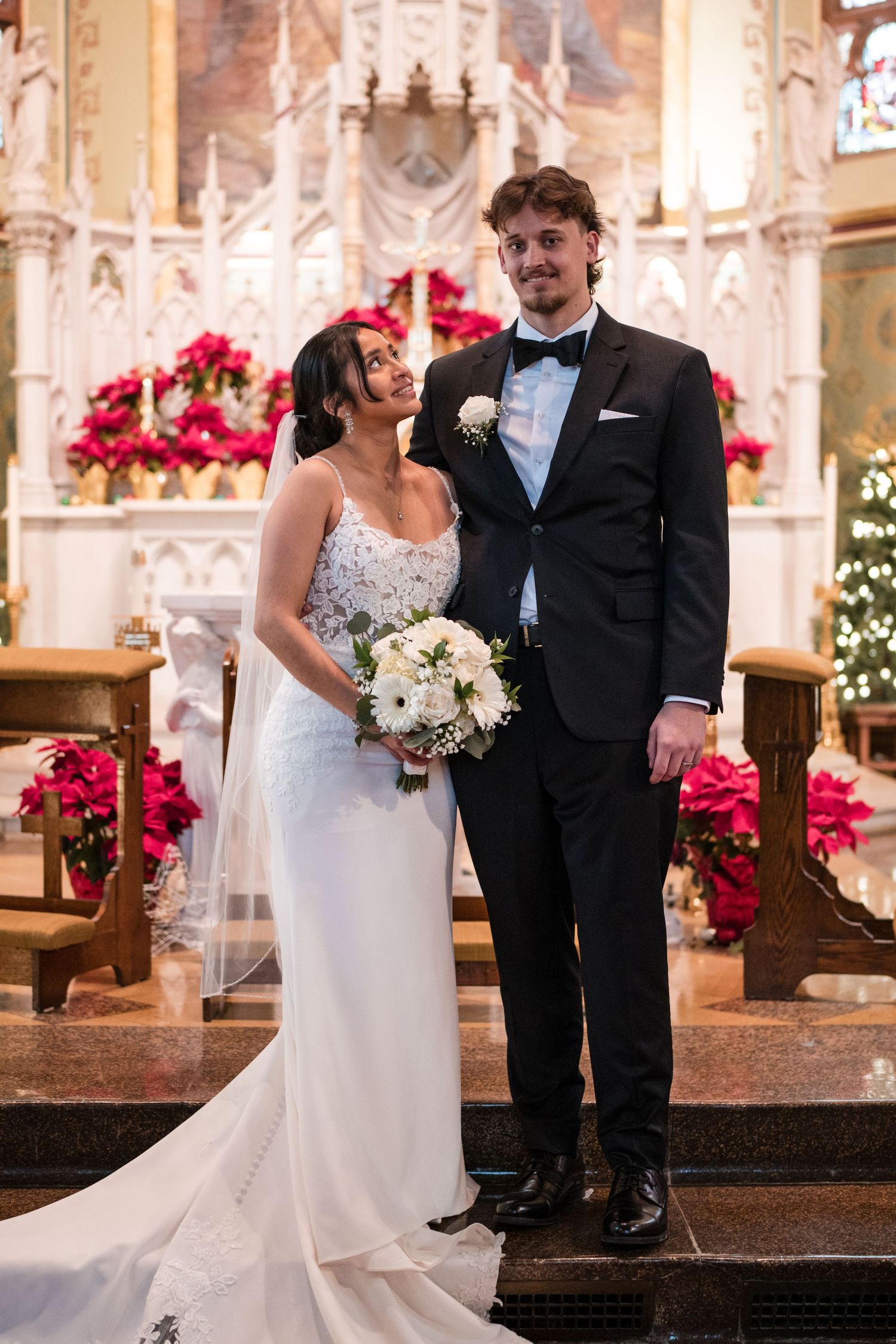 Elegant couple posing at church altar with red poinsettias and holiday decorations.