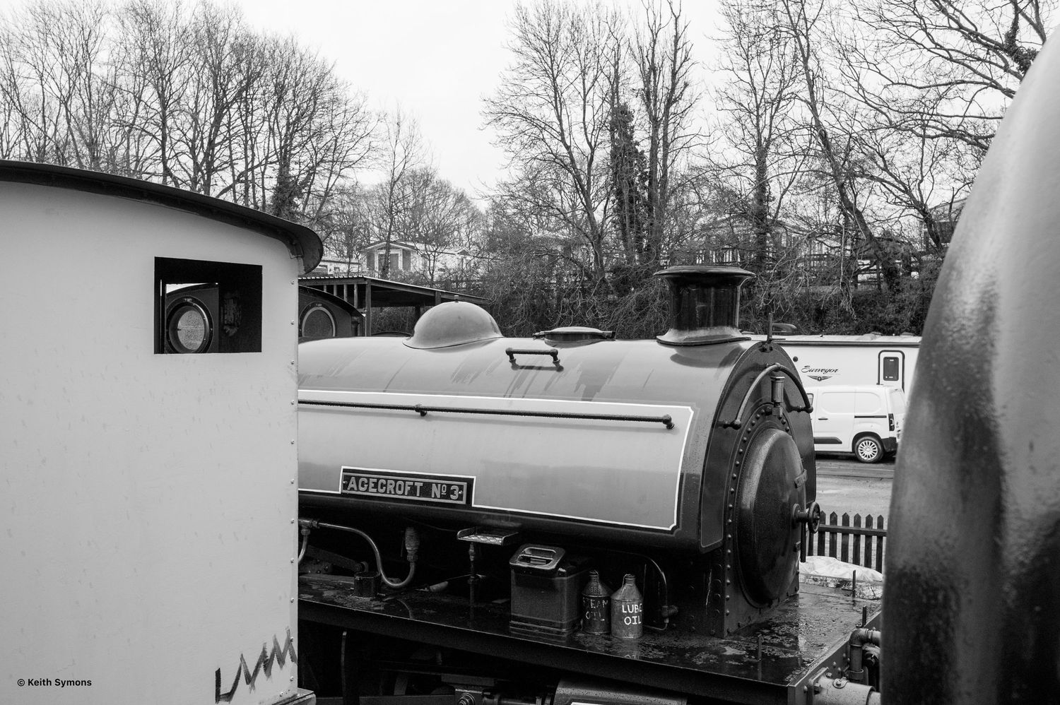 A vintage railway car with curved metallic body sits on tracks in black and white photography.