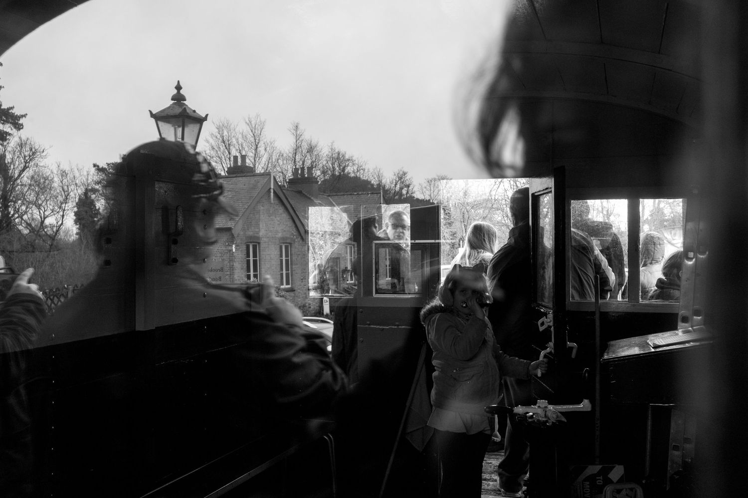 Black and white photo showing passengers boarding a vintage train car, with a station lamp post visible in background.