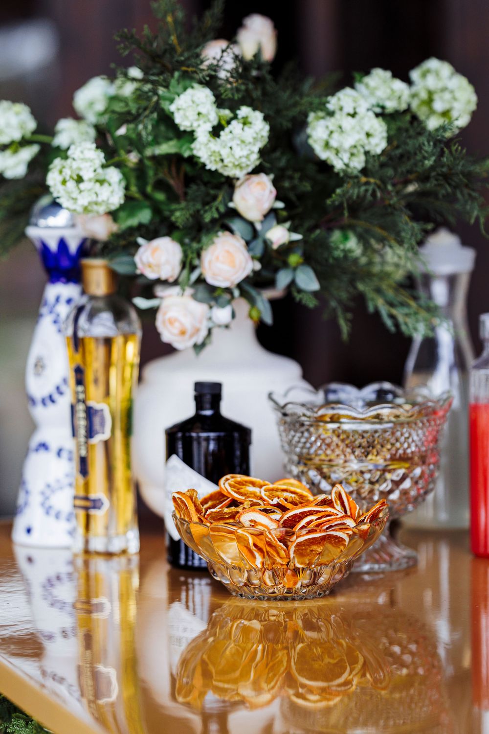 Romantic table setting with peach roses, crystal bowls, and blue and white vases alongside glass bottles.