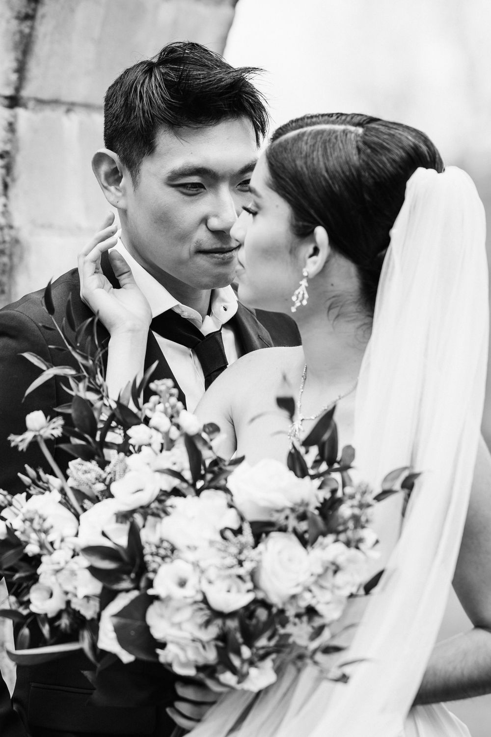 Black and white wedding photo showing intimate moment between newlyweds with bridal bouquet of roses and mixed flowers.