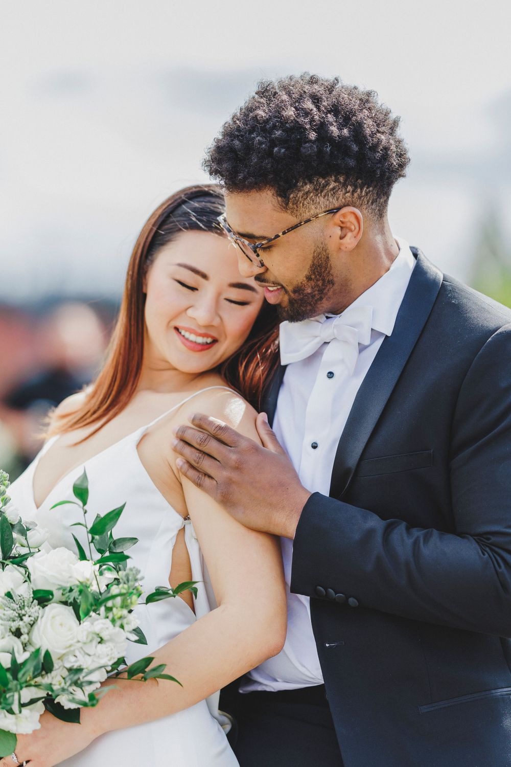Loving couple shares intimate moment at outdoor wedding ceremony with white floral bouquet.