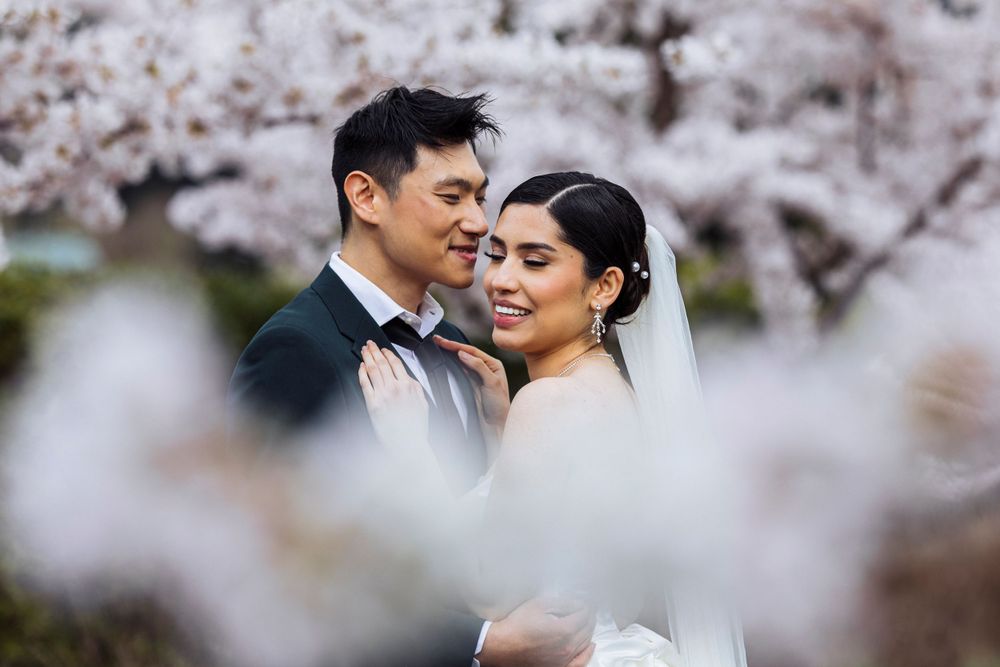 A romantic wedding couple embraces among blooming cherry blossoms in a dreamy spring garden setting.
