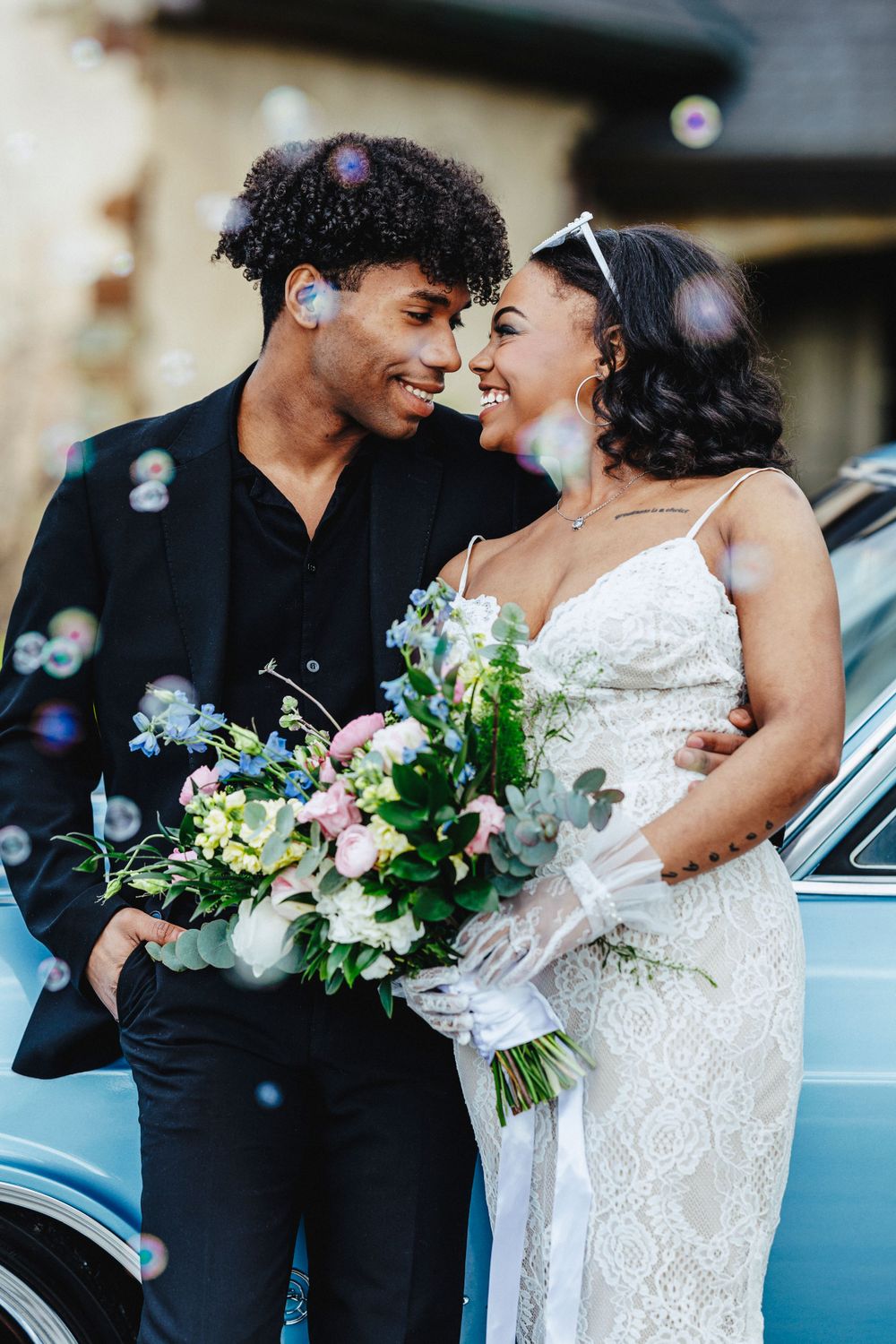 A happy couple share a joyful moment on their wedding day with bubbles floating around and a beautiful floral bouquet.
