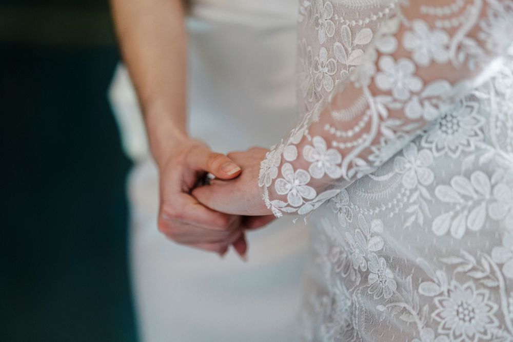 Close-up of holding hands with delicate white lace wedding dress detail in soft focus.
