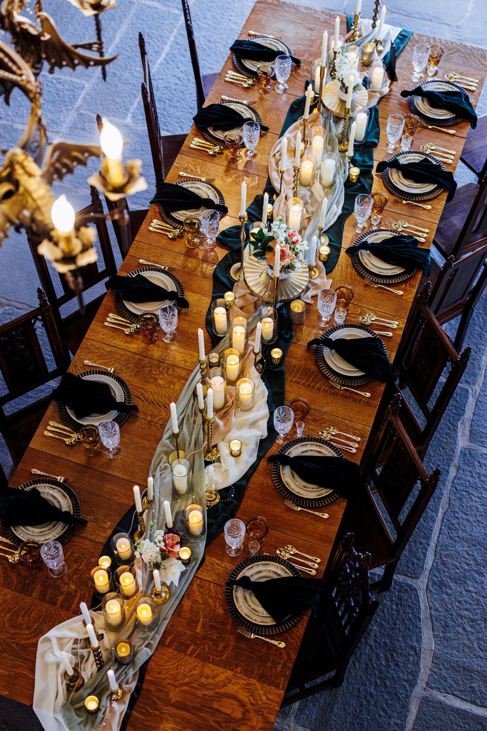Elegant dinner table setting with dark wooden chairs, lit candles and a floral centerpiece running down a long wooden table.