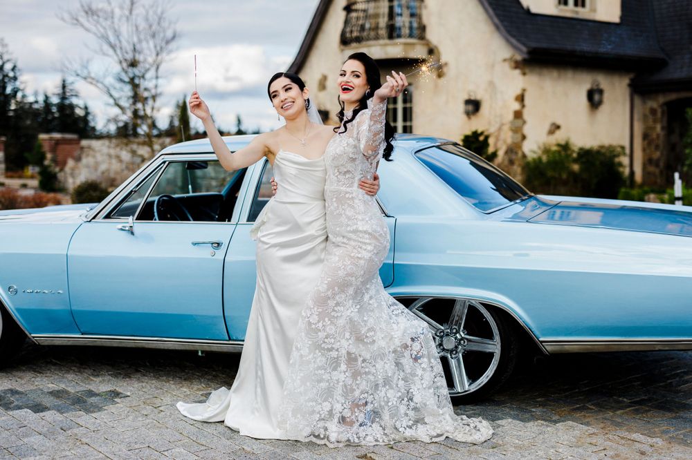 A classic light blue vintage car parked outside an elegant stone house serves as backdrop for a celebratory wedding moment.