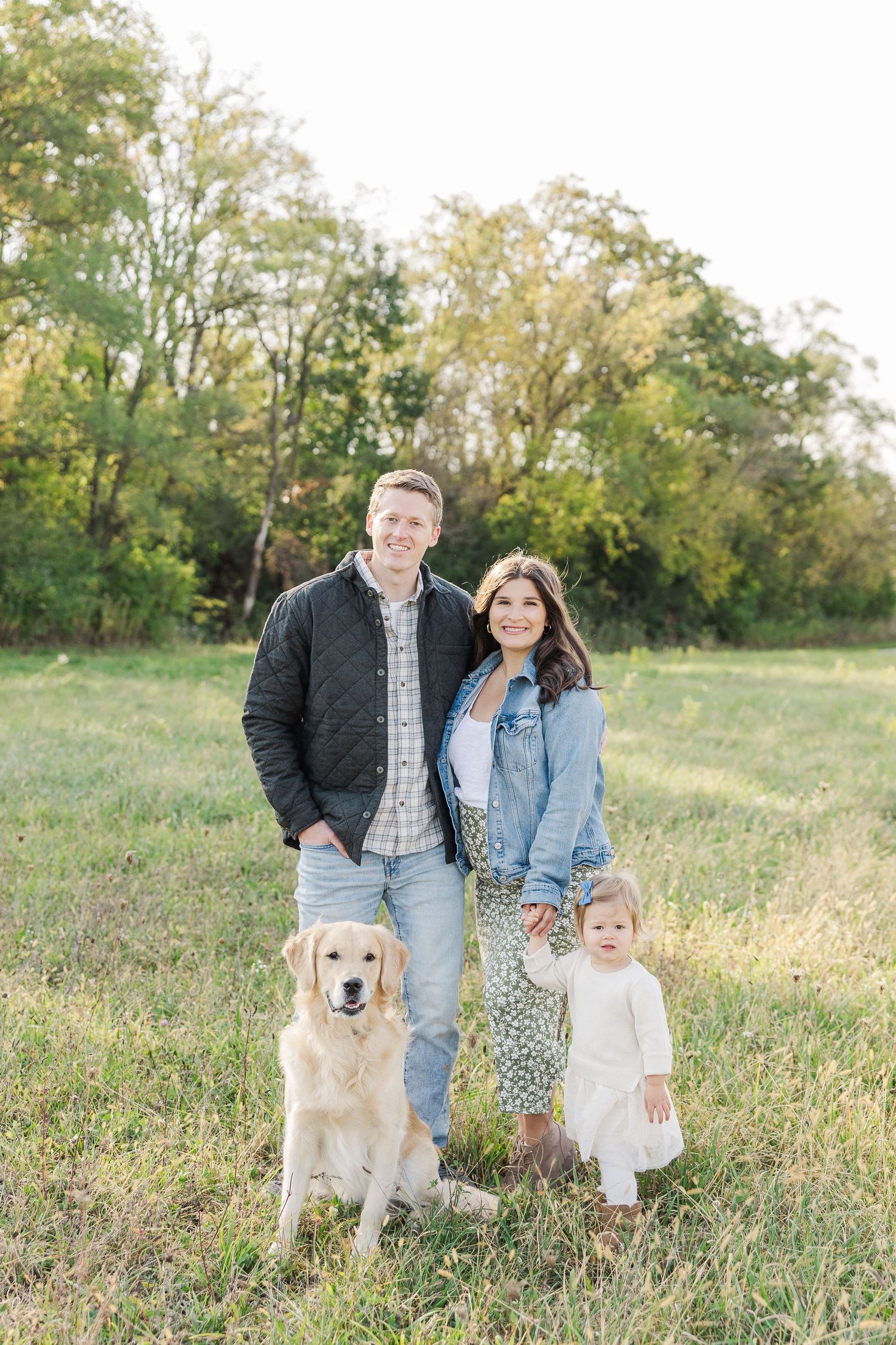 A family stands together in a grassy field during autumn with their golden retriever dog beside them.