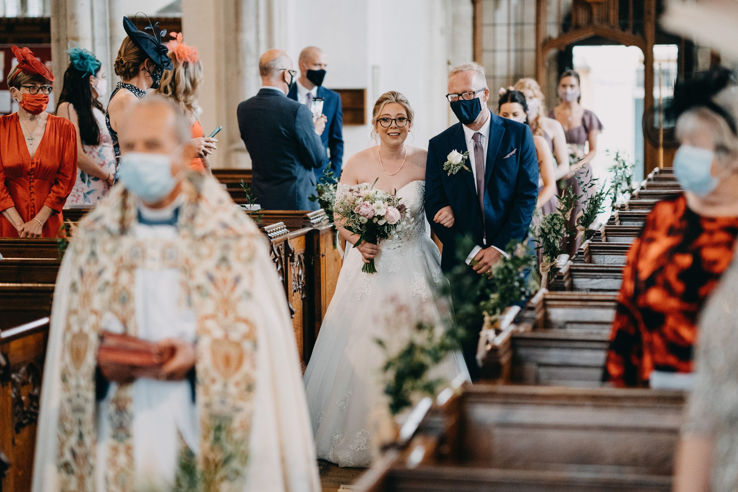 A wedding ceremony processional inside a church with floral decor and masked guests during the pandemic.