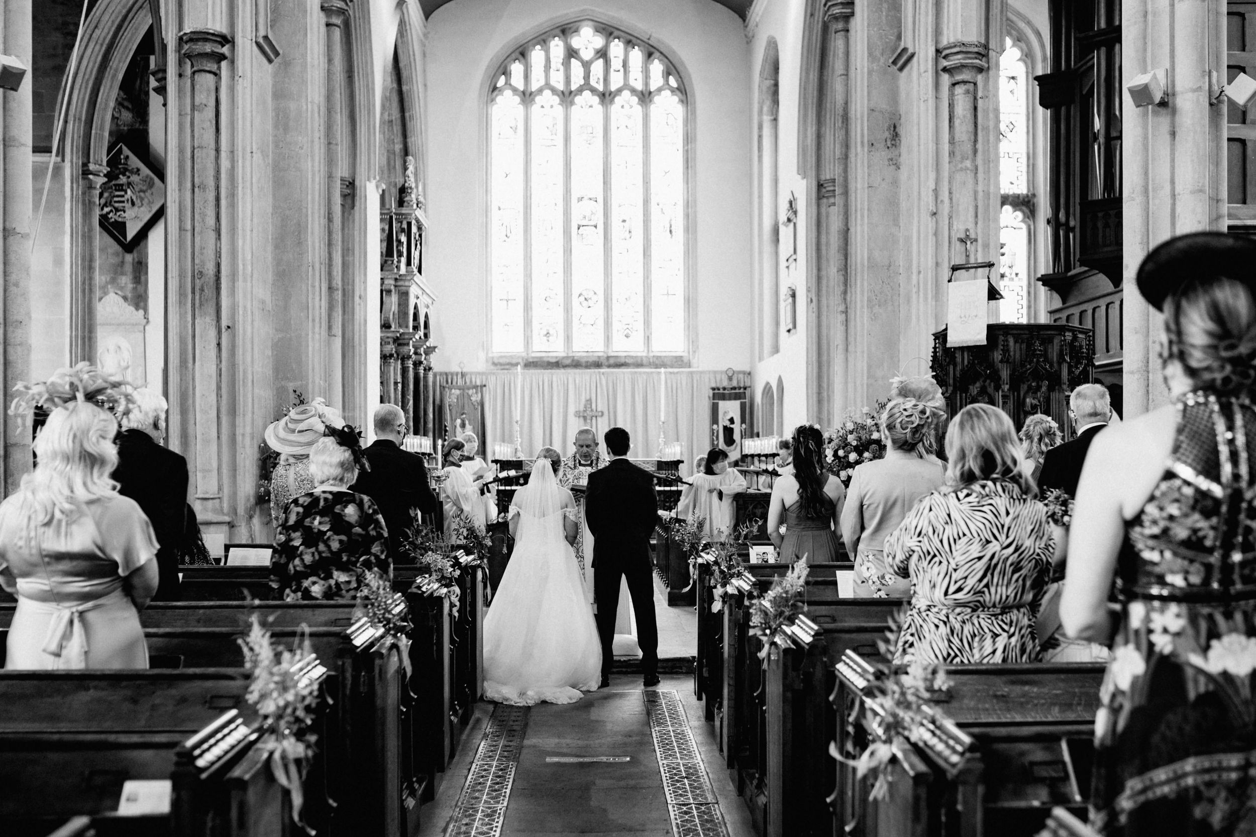 Black and white photo of a wedding ceremony in a traditional church in Stamford with stained glass windows and wooden pews.