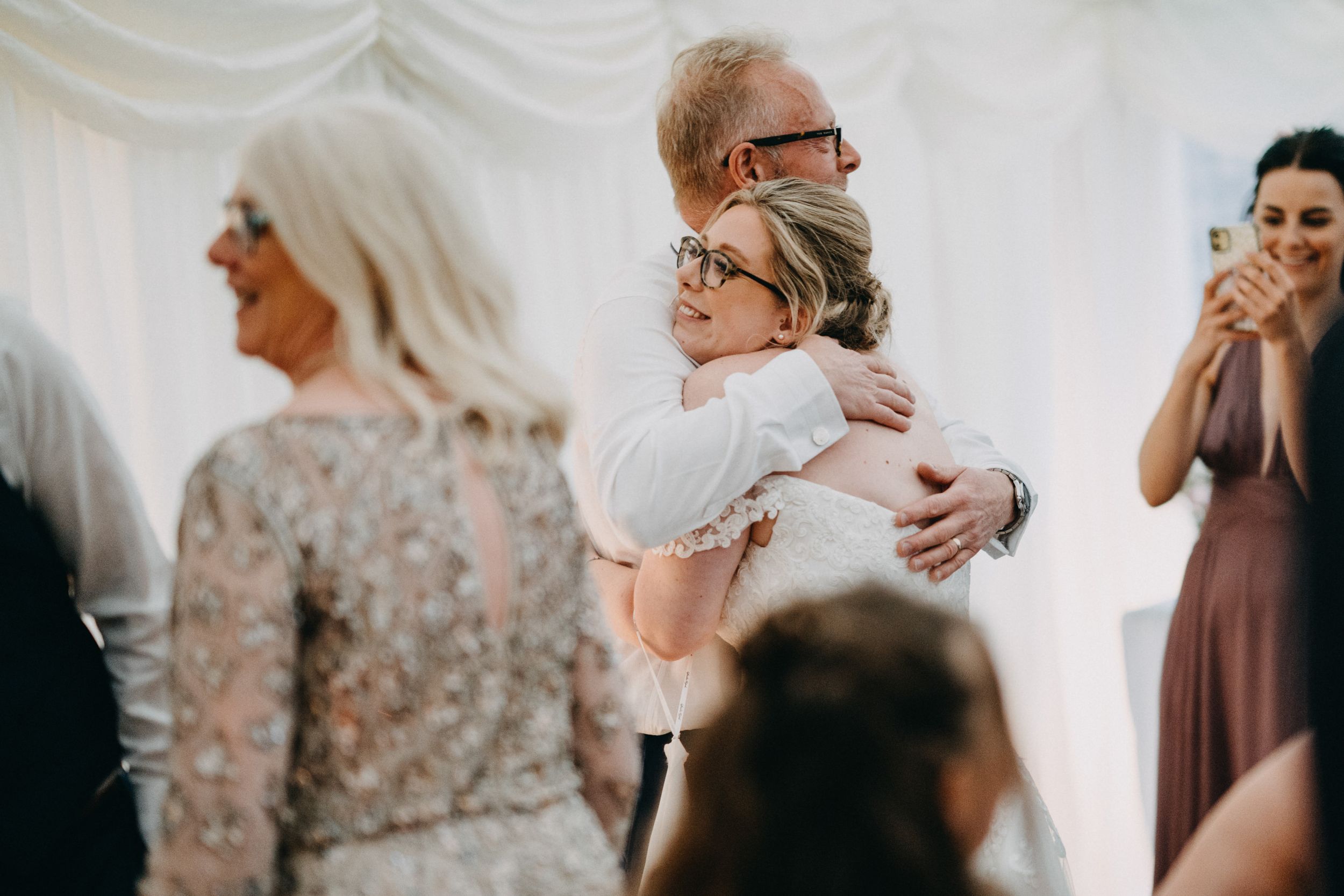 Emotional moment shared between two people embracing during a wedding ceremony as other guests look on.