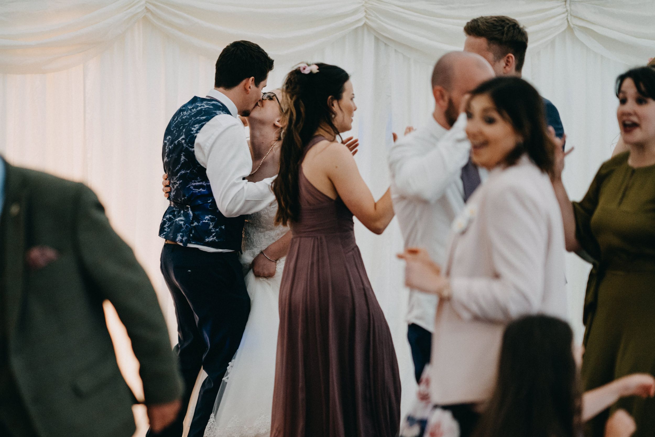 Party guests dancing and socializing during a celebration inside an elegant white tent venue.