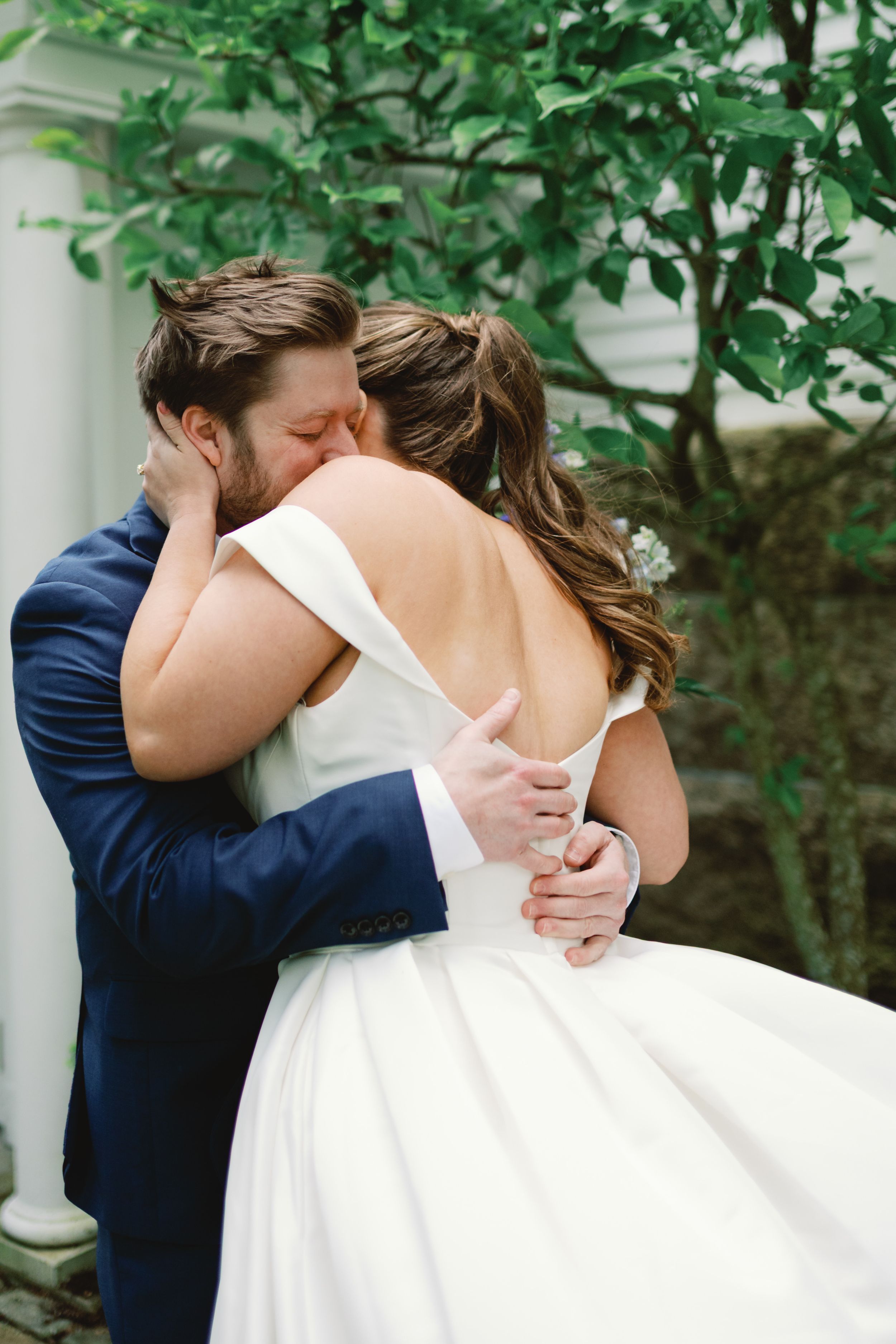 Four romantic wedding photos in sequence showing a couple kissing outdoors with greenery and white pillars visible.