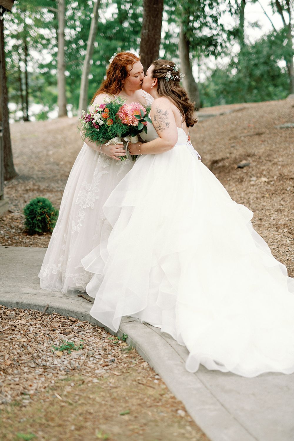Two brides in beautiful white wedding dresses share a joyful moment outdoors.