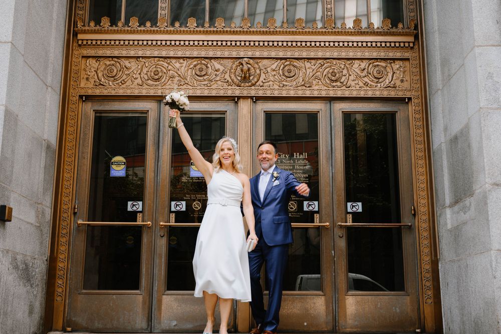 A joyful celebration pose in front of ornate golden doors at a historic building.