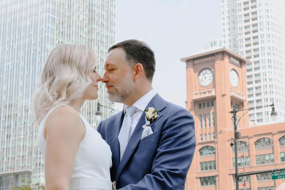 A romantic wedding couple shares an intimate moment in front of a clock tower in the city.