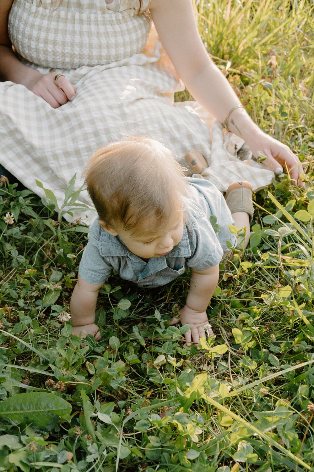 Baby exploring grass and flowers while wearing light blue outfit on picnic blanket.