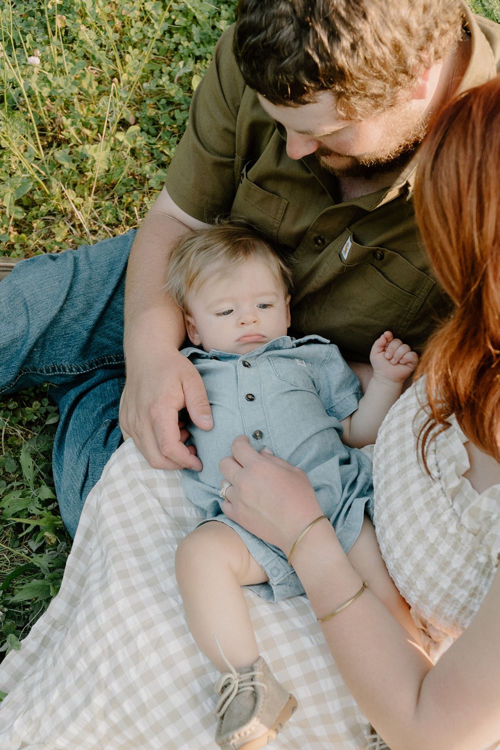 Tender family moment captured on checkered blanket in grassy field.