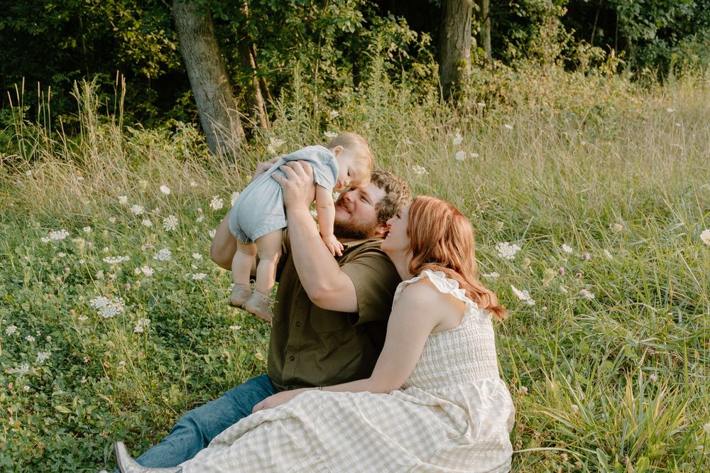 A tender family moment in a sunlit meadow with wildflowers and trees.