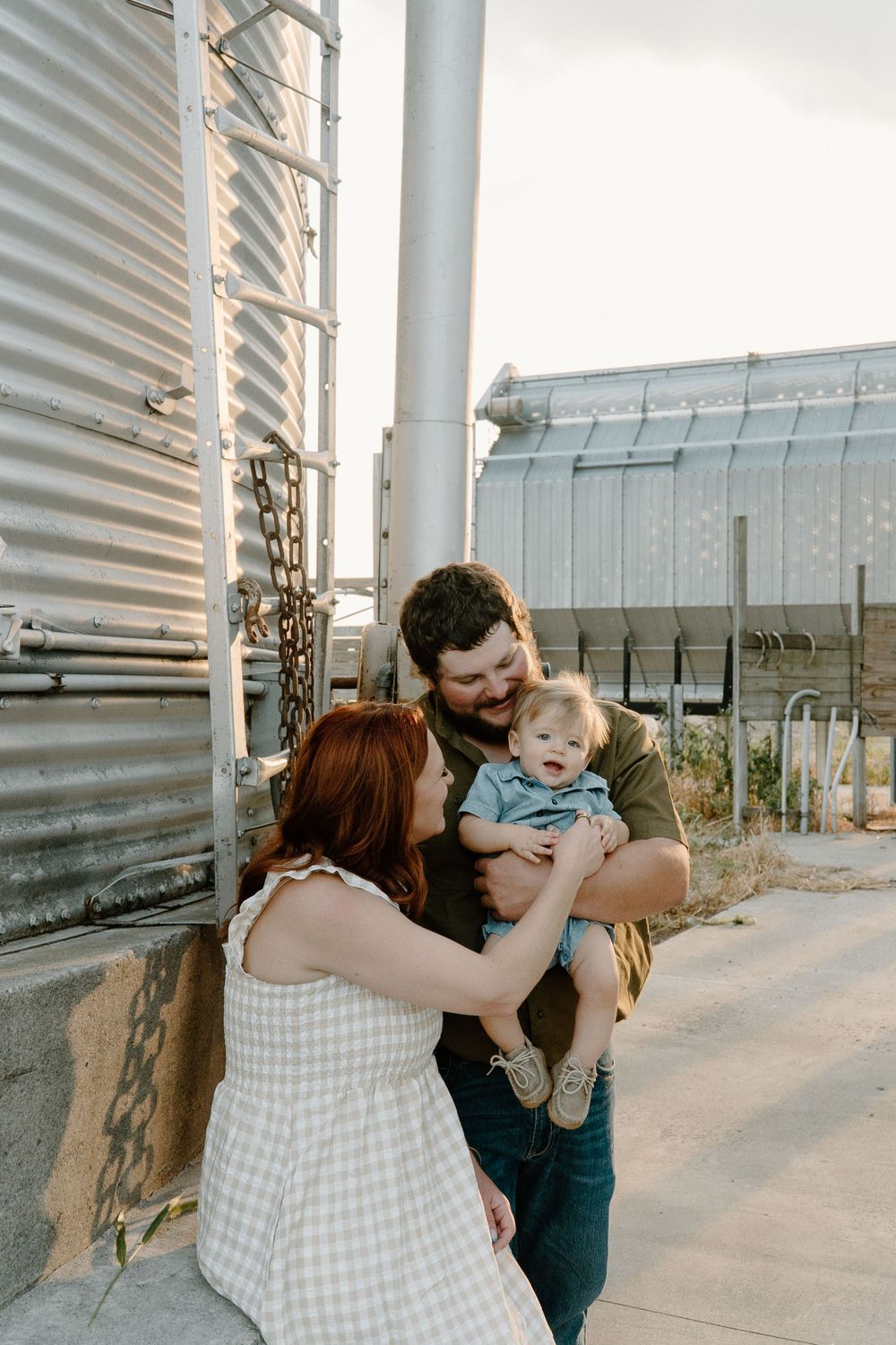 A tender family moment shared beside industrial storage silos at sunset.