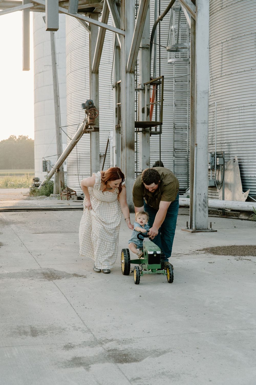 Family enjoying playtime with a toy tractor near grain storage facilities.