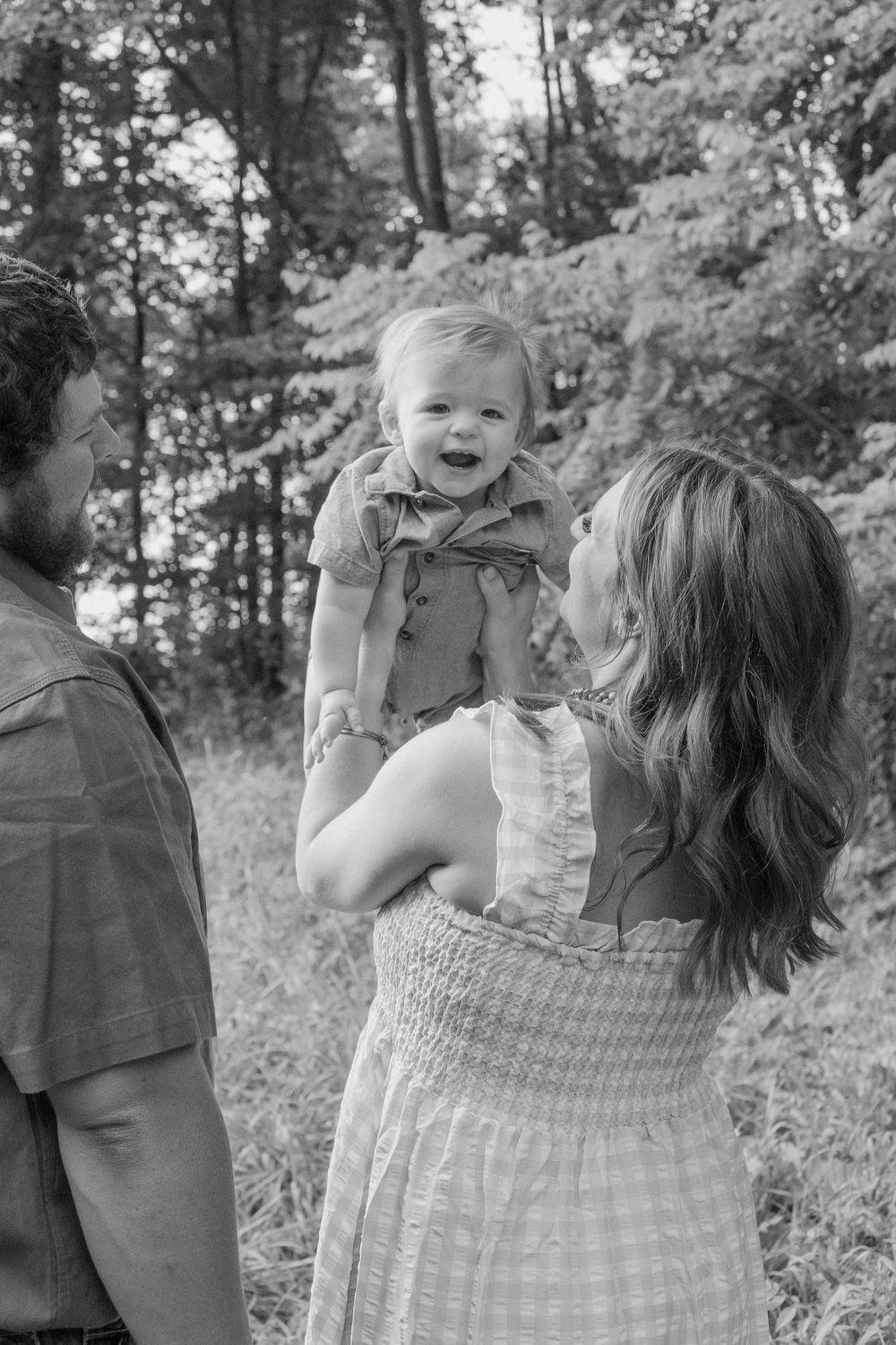 Black and white photo capturing joyful family moment in a wooded setting.