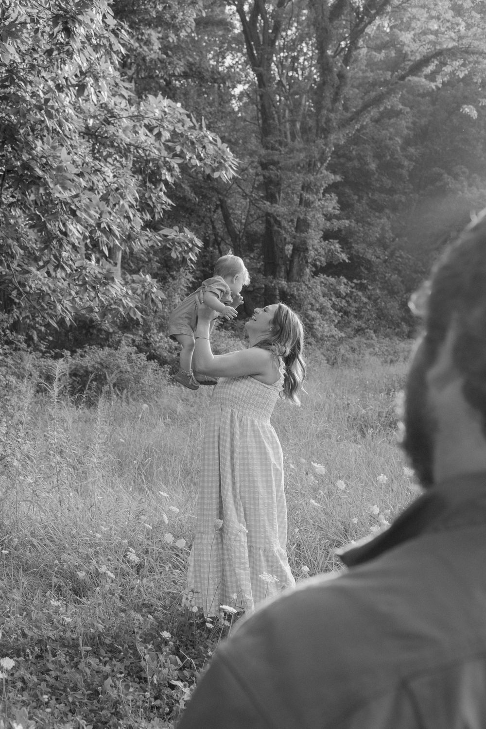 Black and white portrait of a tender family moment in a sunlit meadow.