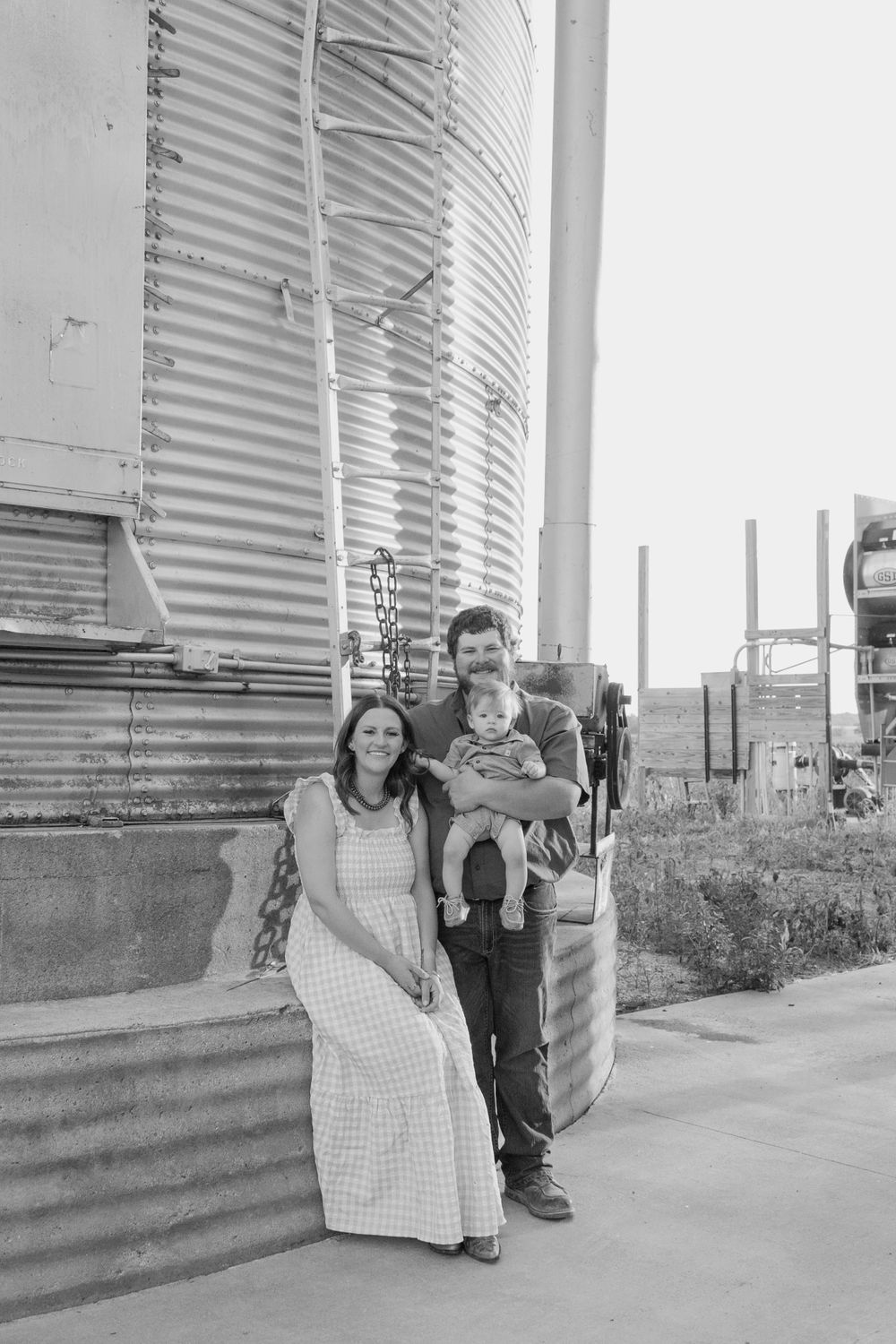 Black and white portrait of family standing together by grain silos.