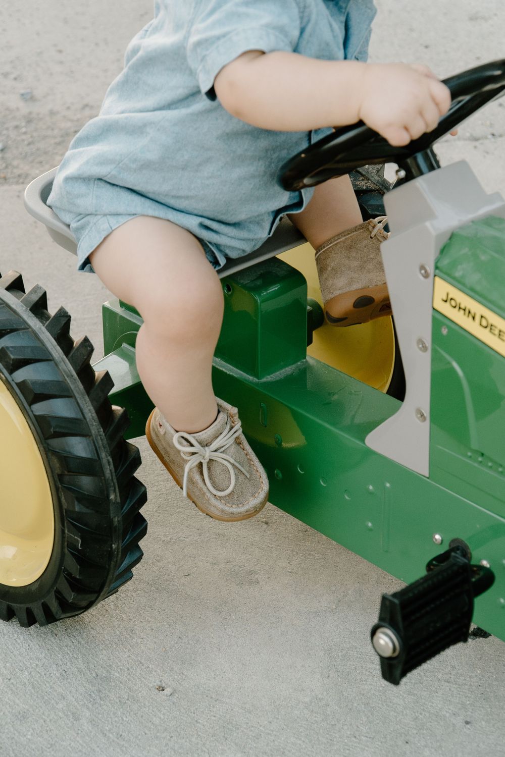 Close-up of small legs and feet on a green John Deere toy tractor.