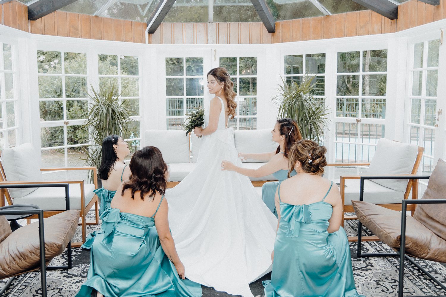 Bridesmaids in turquoise dresses help adjust a flowing white wedding gown captured by Apertured Media Auckland Wedding Photographer.