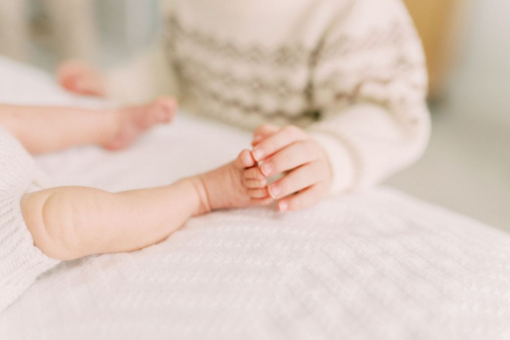 Close up of tiny baby hands grasping gently against white textured fabric.