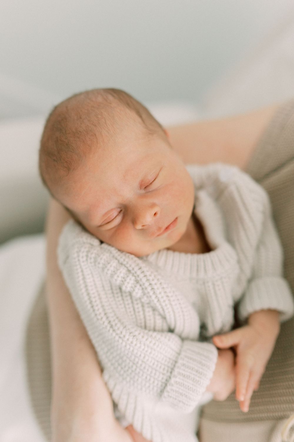A peaceful sleeping newborn wearing a soft white knitted sweater.