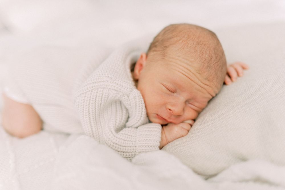 Peaceful sleeping newborn in white knit sweater on soft white bedding.