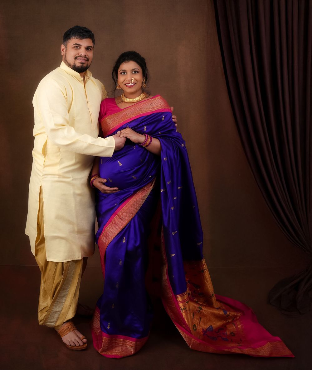 Couple in traditional Indian attire poses against dark curtain backdrop.