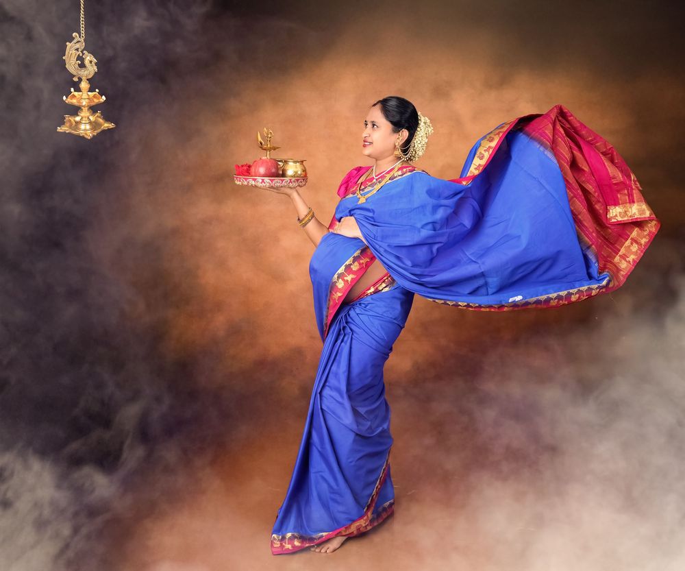 Woman in blue silk saree holds traditional pooja items in dynamic flowing pose.